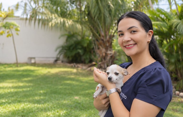 Veterinária da CentroPrev no jardim de uma residência, segurando um cachorro pequeno no colo.